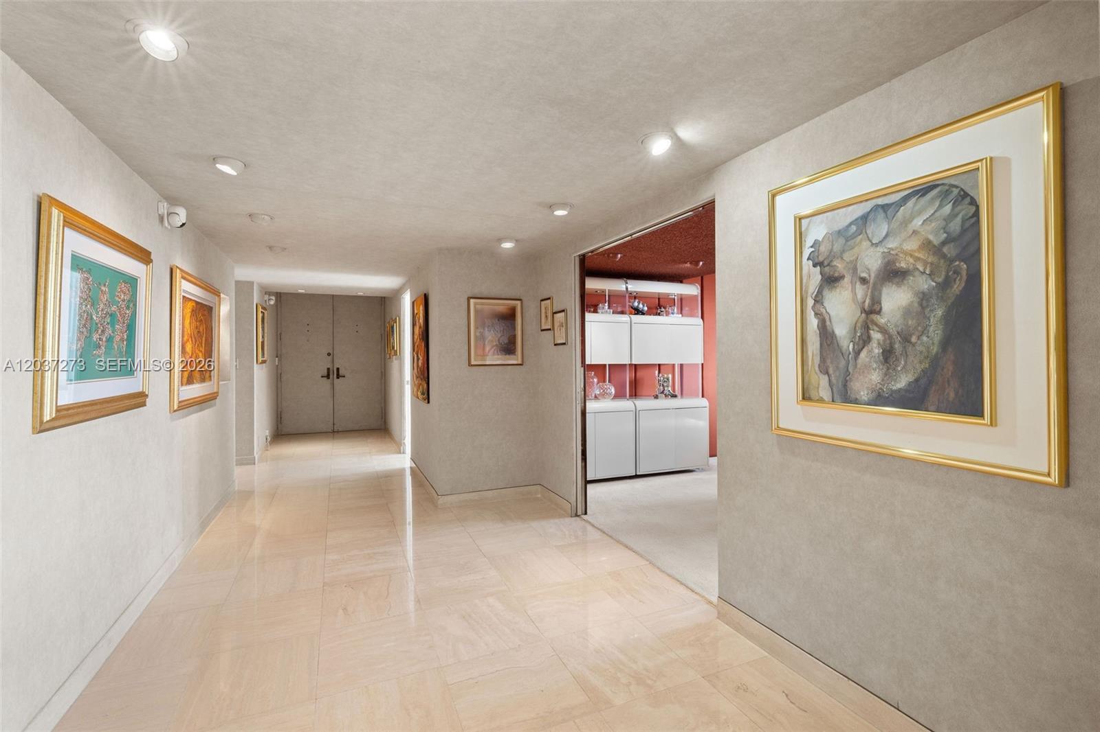 A hallway with light-colored tile flooring and framed artwork leads to a room with cabinets — 5500 Collins Ave # 1401, Miami Beach FL 33140, MIAMI BEACH, FL