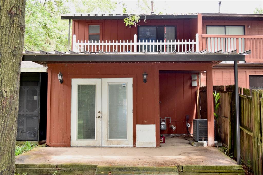 A red-sided townhouse exterior features a ground-level patio, French doors, and an upper-level balcony — 4614 SW 67TH TERRACE, GAINESVILLE, FL