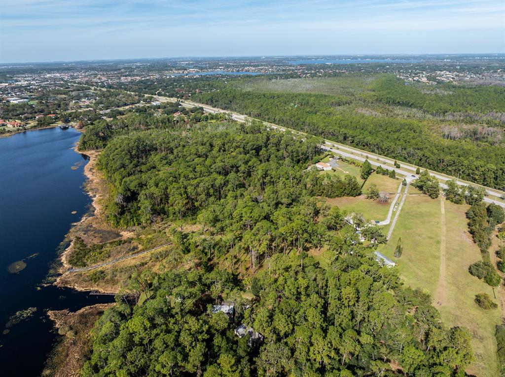 An aerial view shows a wooded property bordering a lake next to a highway — 8834 WINTER GARDEN VINELAND ROAD, ORLANDO, FL