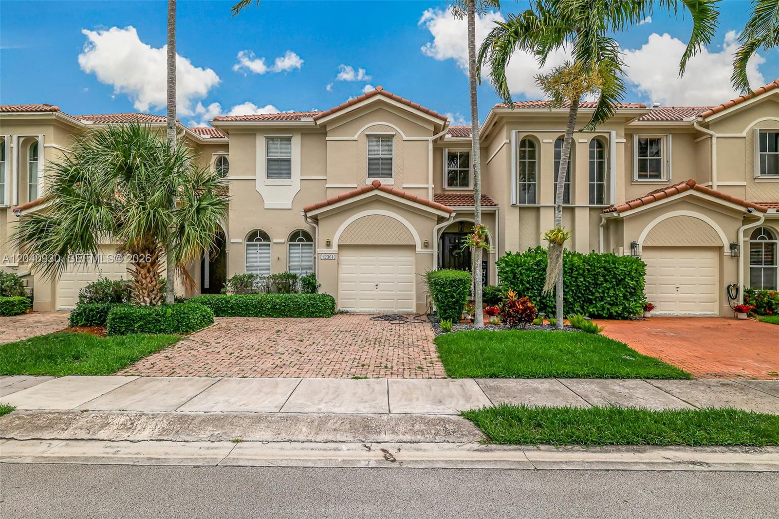 A two-story townhouse with a beige stucco facade, arched windows, and a brick driveway — 12361 SW 123rd Ter, Miami FL 33186, MIAMI, FL