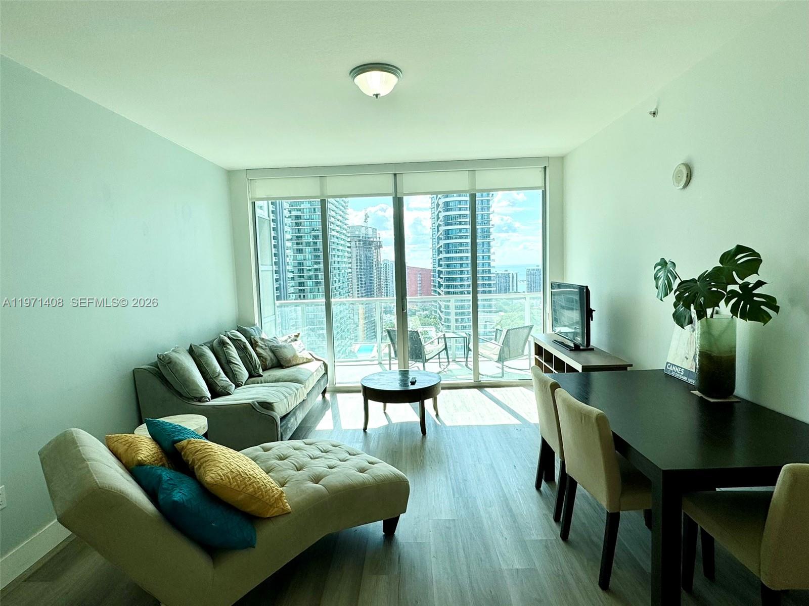 A living and dining area features light wood flooring, a sofa, a chaise, and balcony views — 1111 SW 1st Ave # 3018, Miami FL 33130, MIAMI, FL