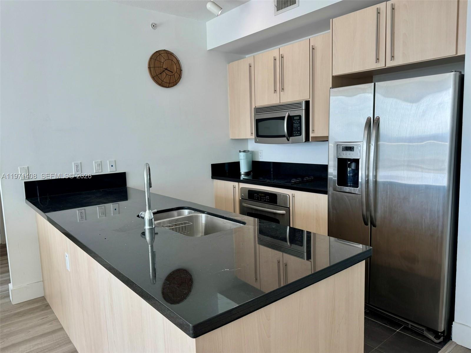 A kitchen features light wood cabinets, black countertops, stainless steel appliances, and a central island — 1111 SW 1st Ave # 3018, Miami FL 33130, MIAMI, FL