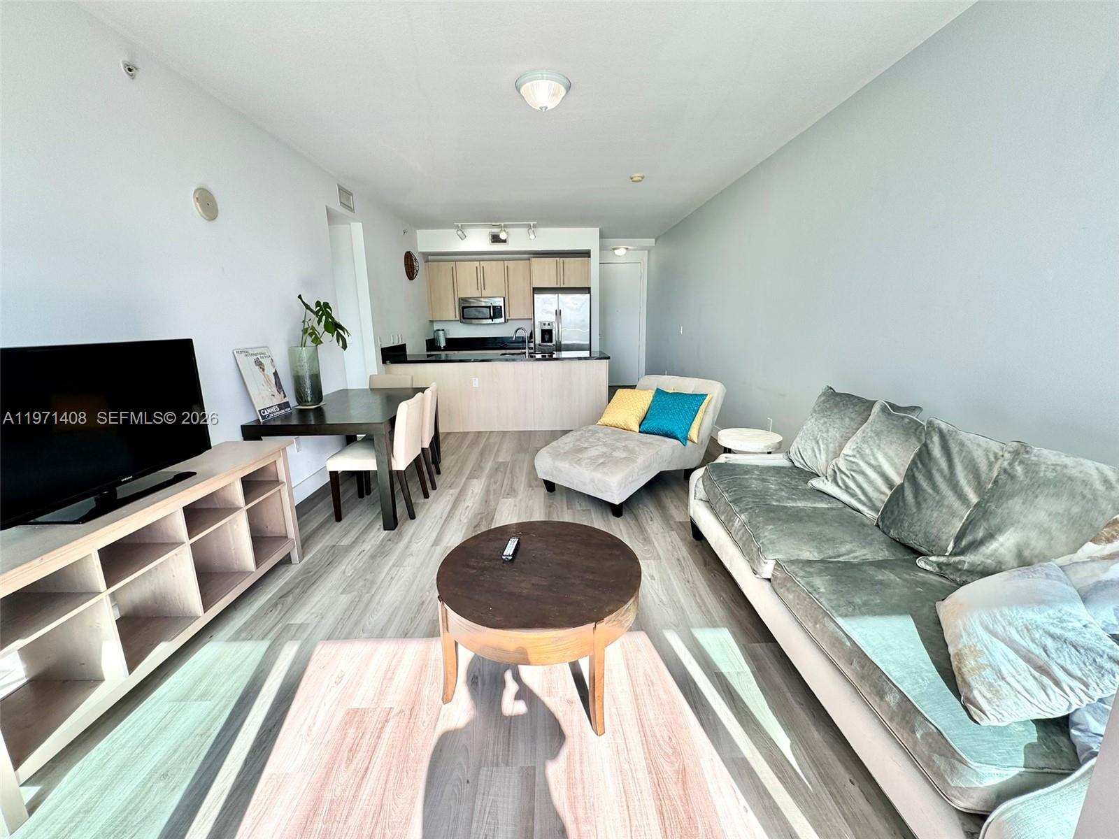 A living room and kitchen area with light wood flooring, a sofa, and a dining table — 1111 SW 1st Ave # 3018, Miami FL 33130, MIAMI, FL