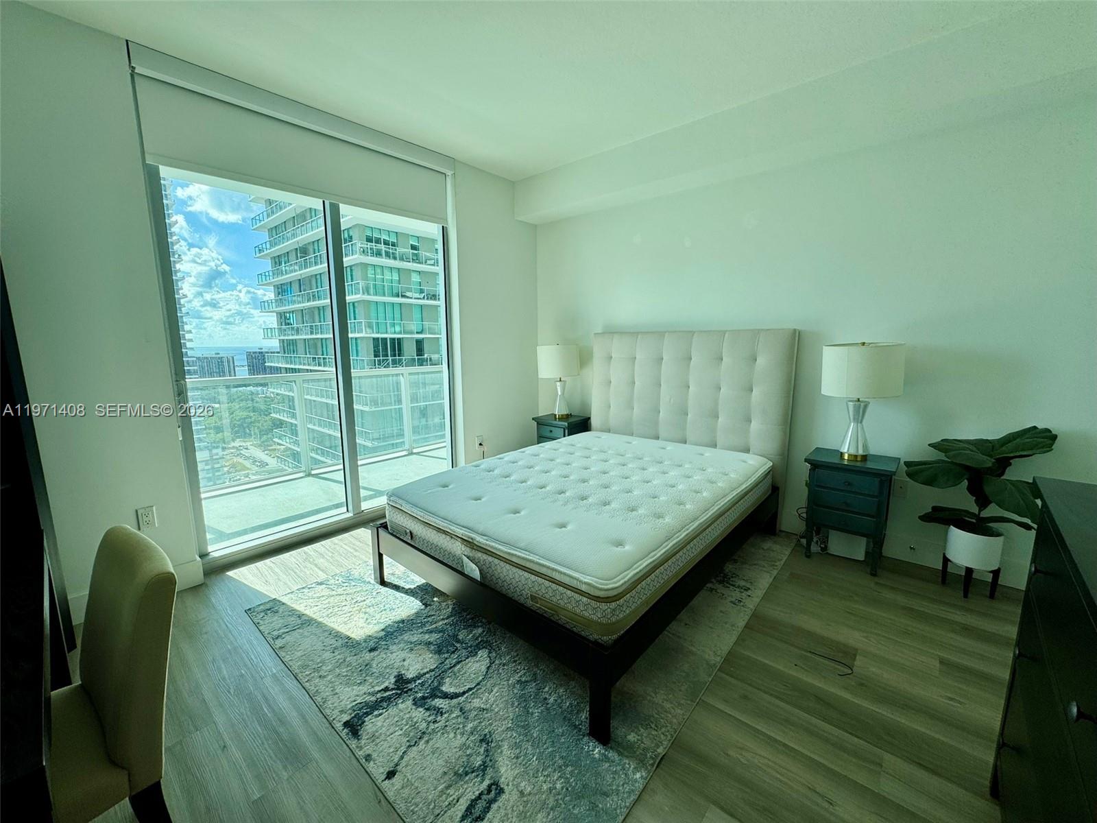 A bedroom with a bed, two nightstands, and a balcony overlooking high-rise buildings — 1111 SW 1st Ave # 3018, Miami FL 33130, MIAMI, FL
