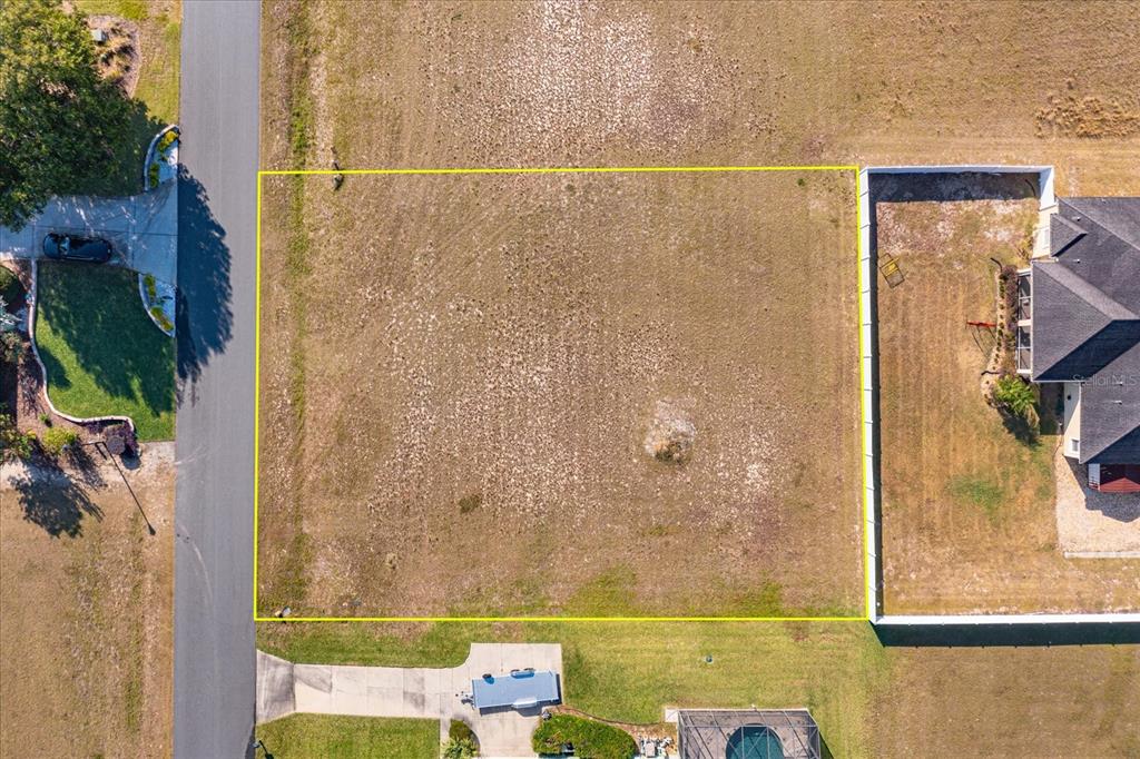 An aerial view shows a vacant rectangular residential lot outlined in yellow next to houses — 1112 MYRTLE BREEZES COURT, FRUITLAND PARK, FL
