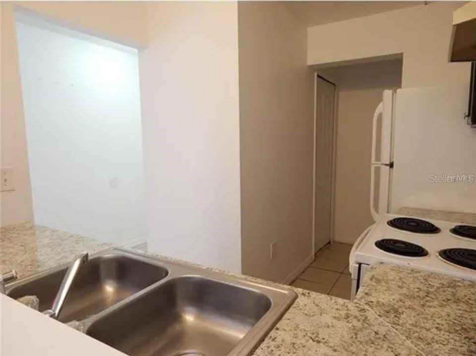 A kitchen features a double-basin stainless steel sink, granite countertops, and a white electric stove — 5220 VIA HACIENDA UNIT 212, ORLANDO, FL
