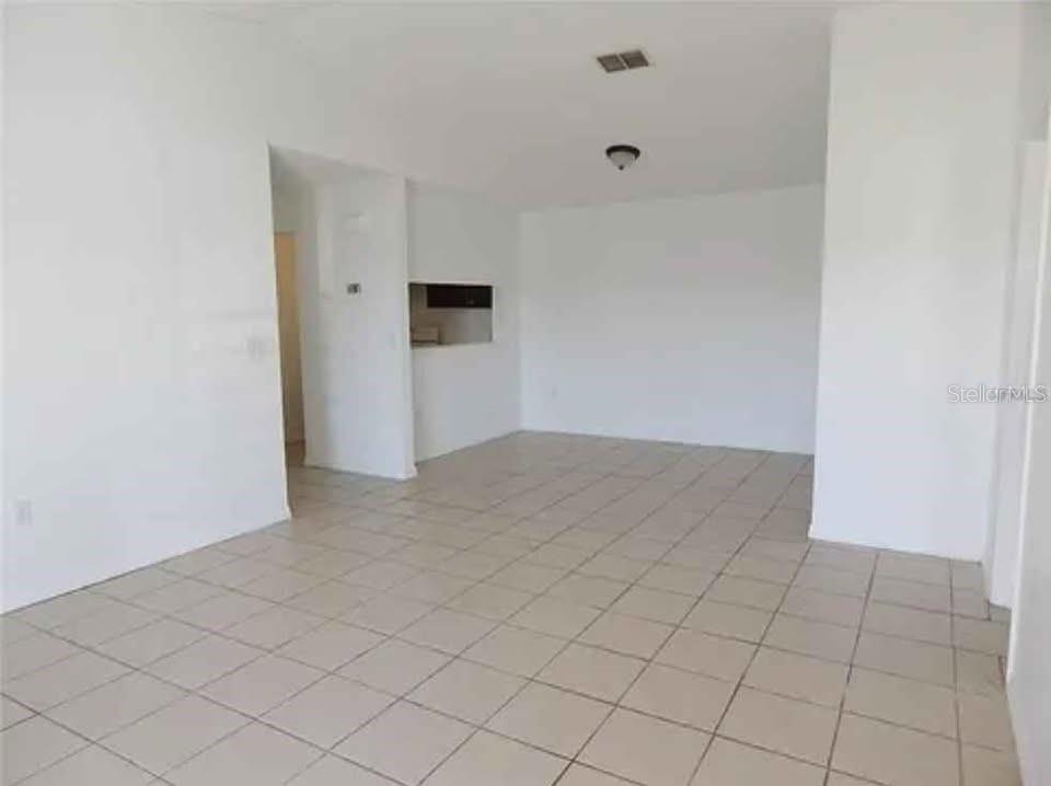 An empty room with white walls and light-colored tile flooring features a kitchen pass-through window — 5220 VIA HACIENDA UNIT 212, ORLANDO, FL