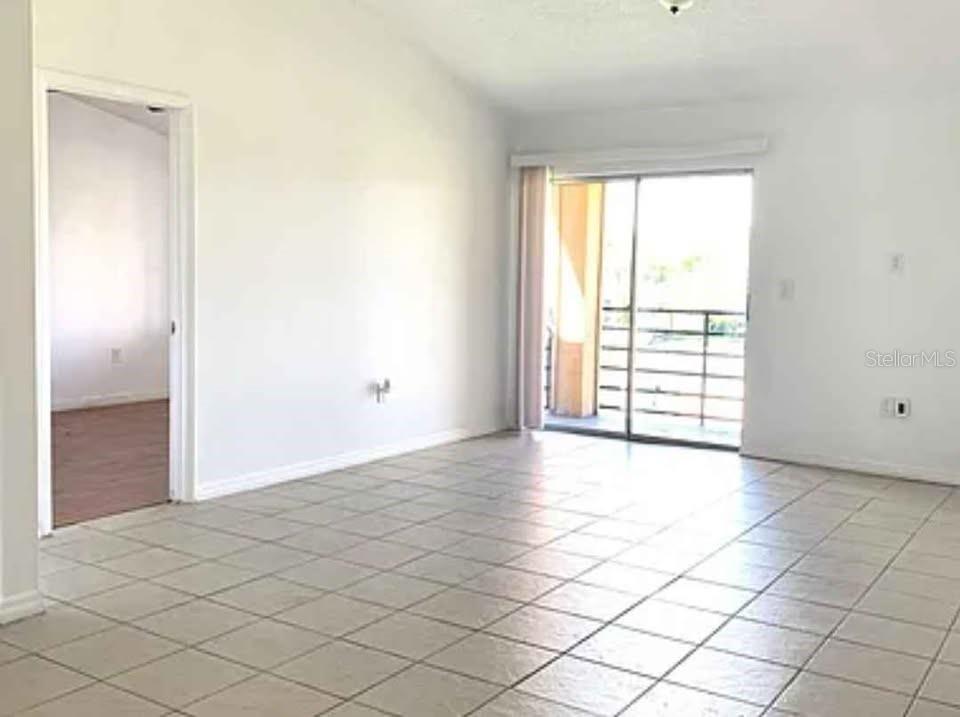 An empty living room features light-colored floor tiles, white walls, and a sliding glass door — 5220 VIA HACIENDA UNIT 212, ORLANDO, FL