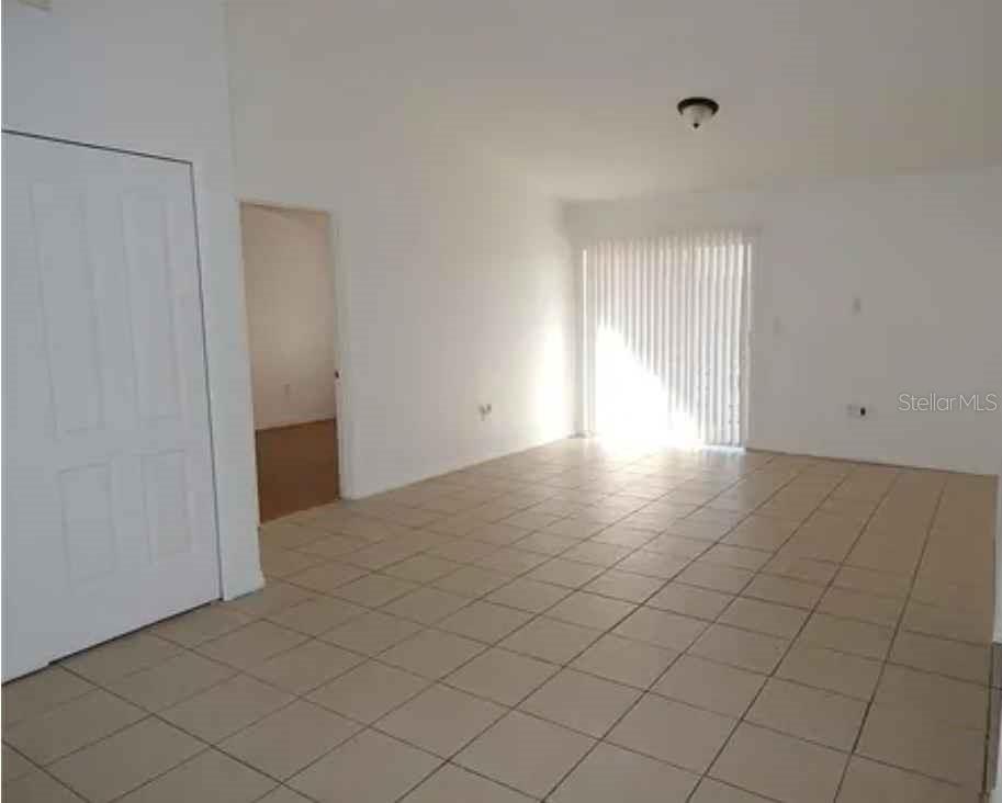 An empty room features white walls, light-colored tile flooring, and a sliding glass door — 5220 VIA HACIENDA UNIT 212, ORLANDO, FL