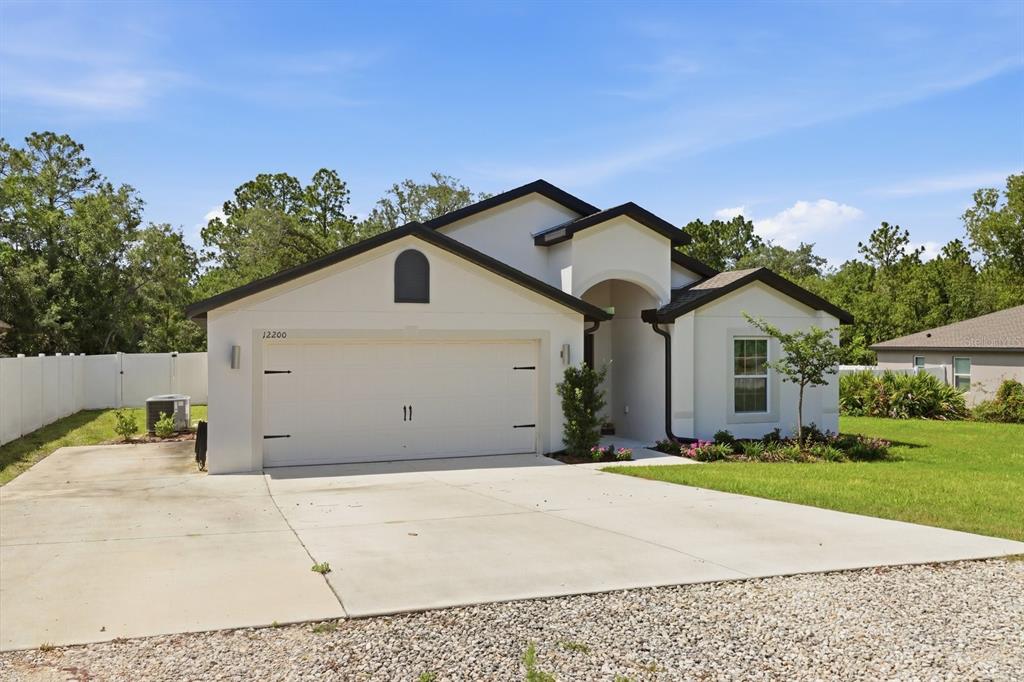 A single-story white house with a two-car garage and a concrete driveway — 12200 PINE FINCH AVENUE, WEEKI WACHEE, FL
