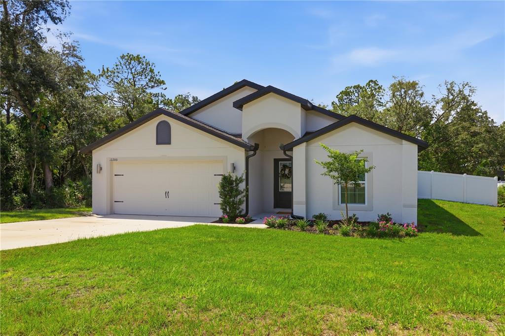 A single-story house with a white stucco exterior, a two-car garage, and a front entrance — 12200 PINE FINCH AVENUE, WEEKI WACHEE, FL
