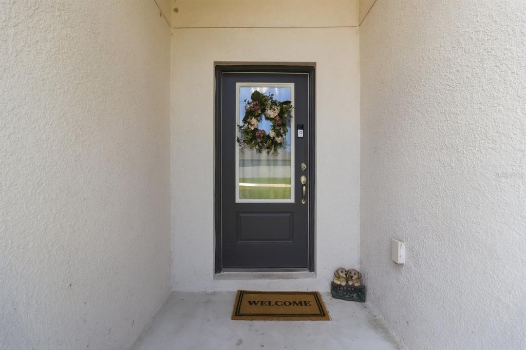 A dark gray front door with a glass insert and wreath sits in a stucco entryway — 12200 PINE FINCH AVENUE, WEEKI WACHEE, FL