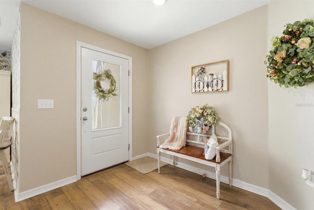 An entryway features a white front door, a wooden bench, and floral wall decor — 12200 PINE FINCH AVENUE, WEEKI WACHEE, FL