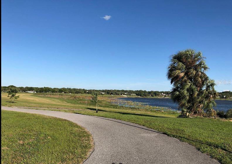 A paved walking path winds through a grassy park toward a lake and palm tree — N/A, LAKE WALES, FL