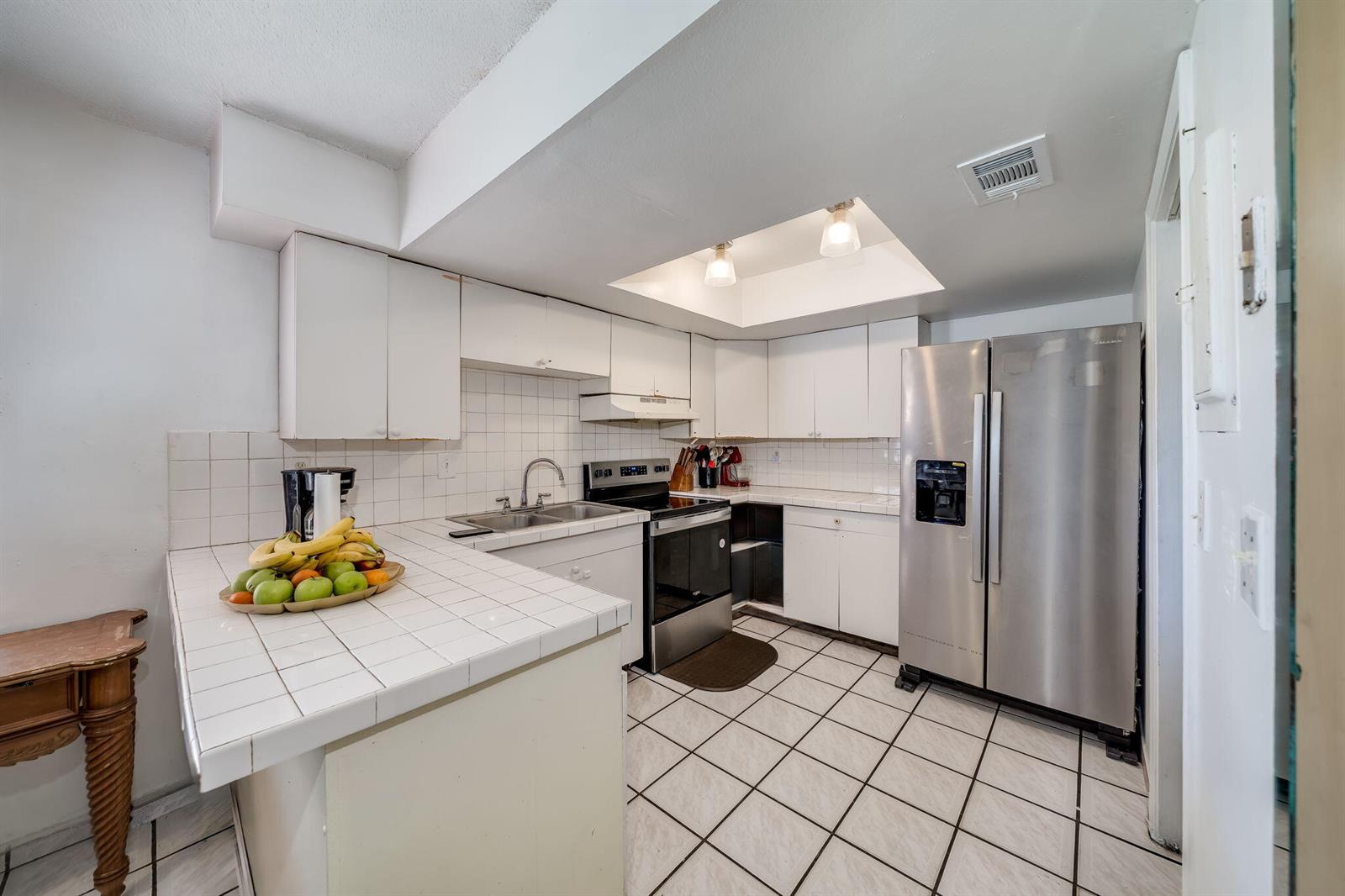 A kitchen features white cabinets, tiled countertops, stainless steel appliances, and white floor tiles — 7 Ann Lee Lane, Tamarac FL 33319, TAMARAC, FL