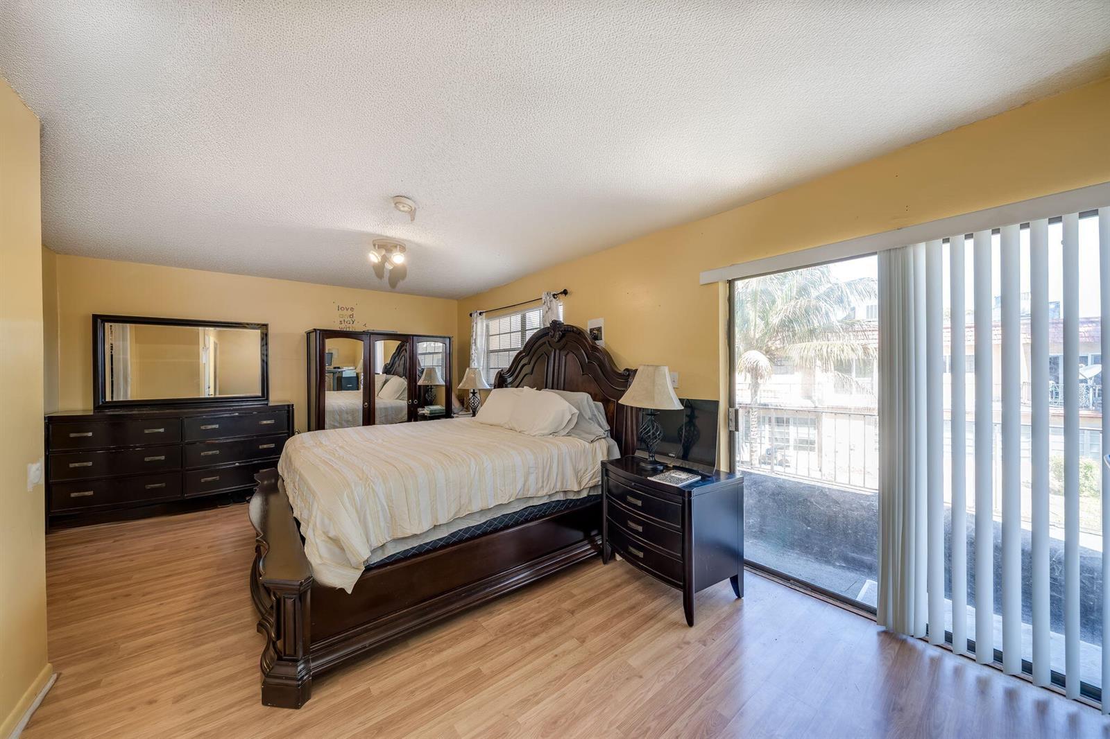A bedroom with yellow walls, wood-look flooring, a dark wood bed frame, and sliding glass doors — 7 Ann Lee Lane, Tamarac FL 33319, TAMARAC, FL