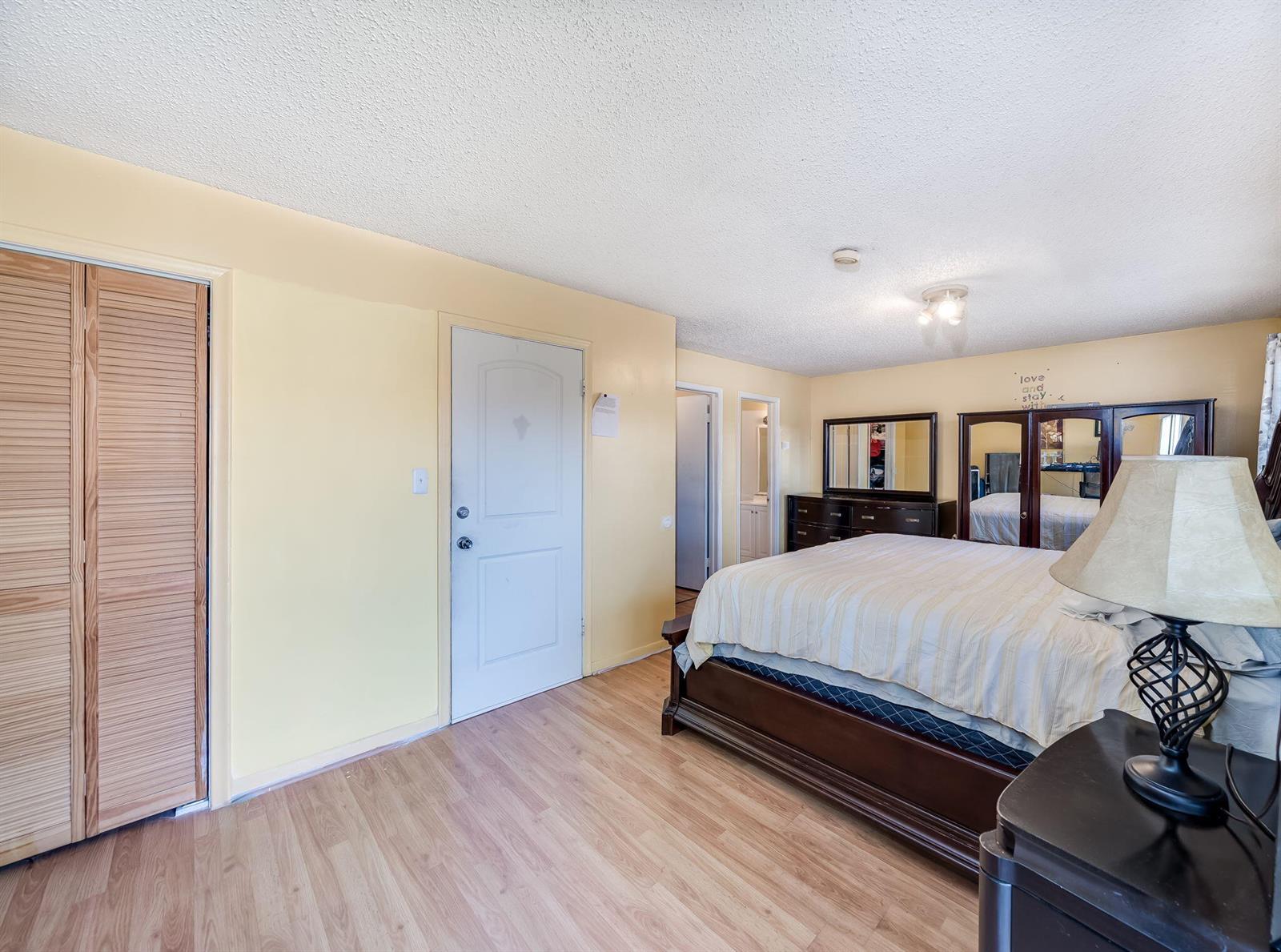 A bedroom features yellow walls, wood-look flooring, a bed with a dark frame, and closet doors — 7 Ann Lee Lane, Tamarac FL 33319, TAMARAC, FL