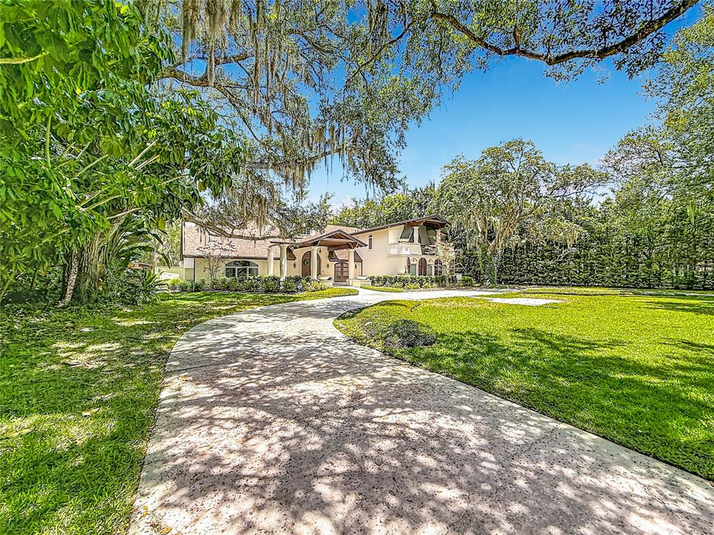 A concrete driveway leads to a two-story house surrounded by large trees and green lawns — 1850 OAK CREEK DRIVE, DUNEDIN, FL