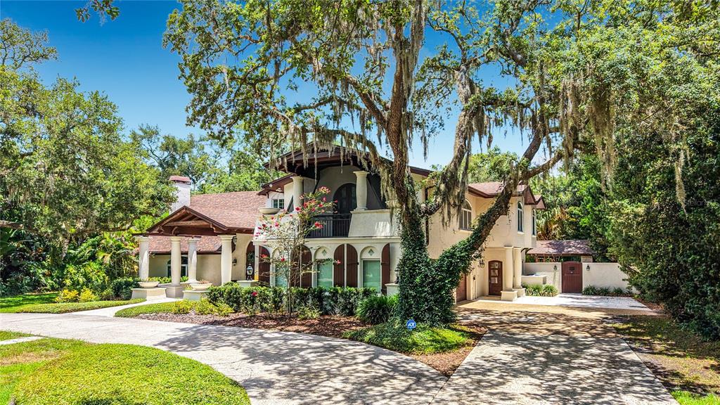 A two-story house with a circular driveway, large oak trees, and a covered front porch — 1850 OAK CREEK DRIVE, DUNEDIN, FL