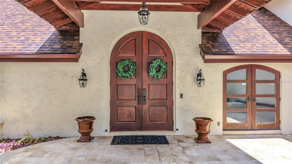 An arched double front door with wreaths sits between two lanterns and large planters — 1850 OAK CREEK DRIVE, DUNEDIN, FL