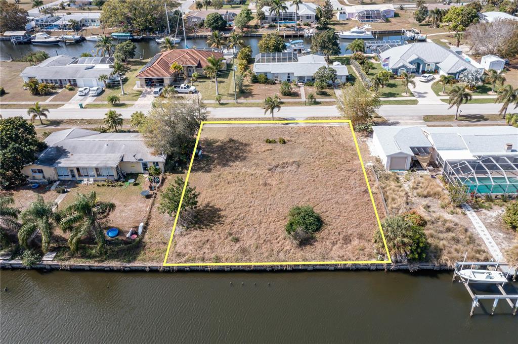 An aerial view shows a vacant waterfront lot outlined in yellow between two residential houses — 109 BALDWIN COURT SE, PORT CHARLOTTE, FL