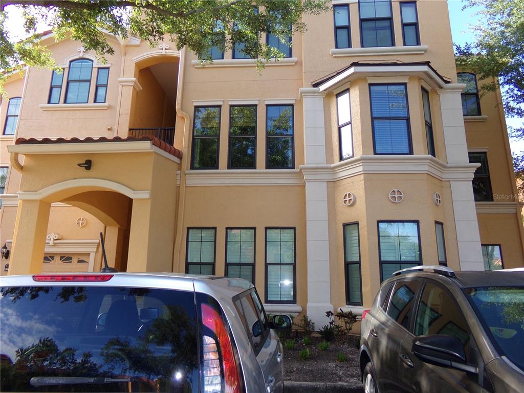 A multi-story tan stucco building exterior features dark-framed windows and two parked cars — 2723 VIA CAPRI UNIT 821, CLEARWATER, FL