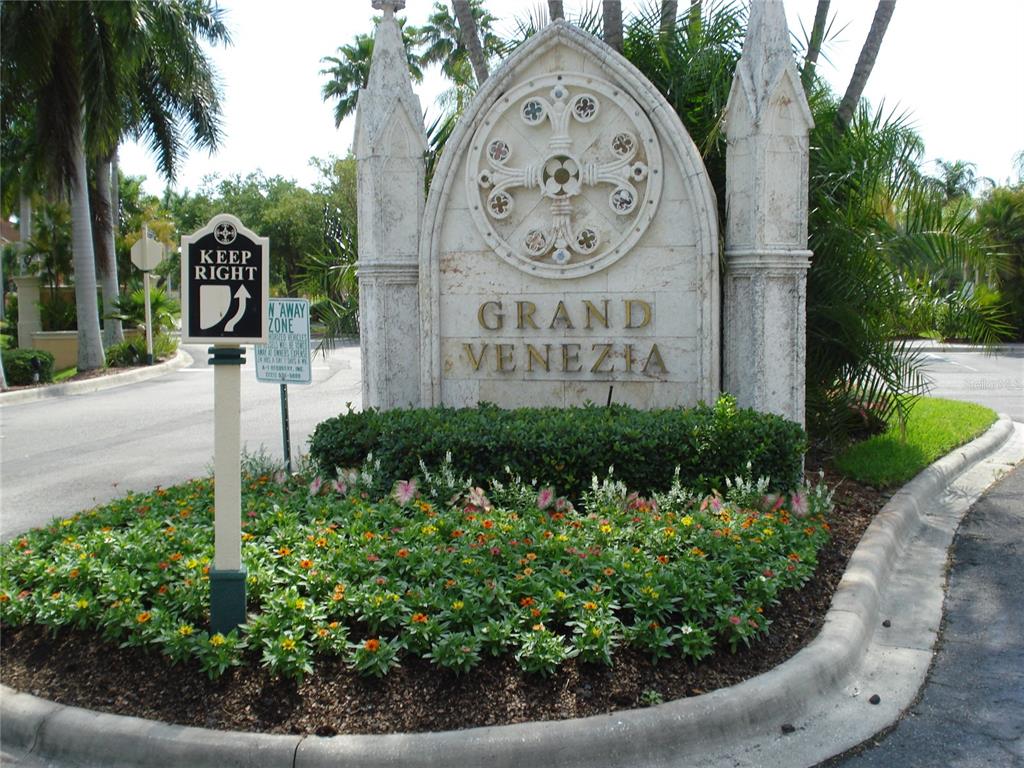 A stone monument sign for Grand Venezia stands in a landscaped traffic island — 2723 VIA CAPRI UNIT 821, CLEARWATER, FL