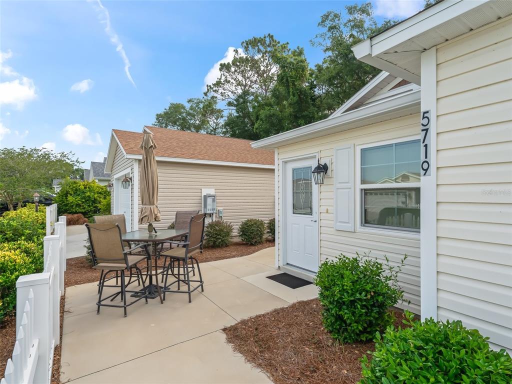 A patio with a table and chairs sits beside a house with light-colored siding — 5719 SPARTINA TERRACE, THE VILLAGES, FL