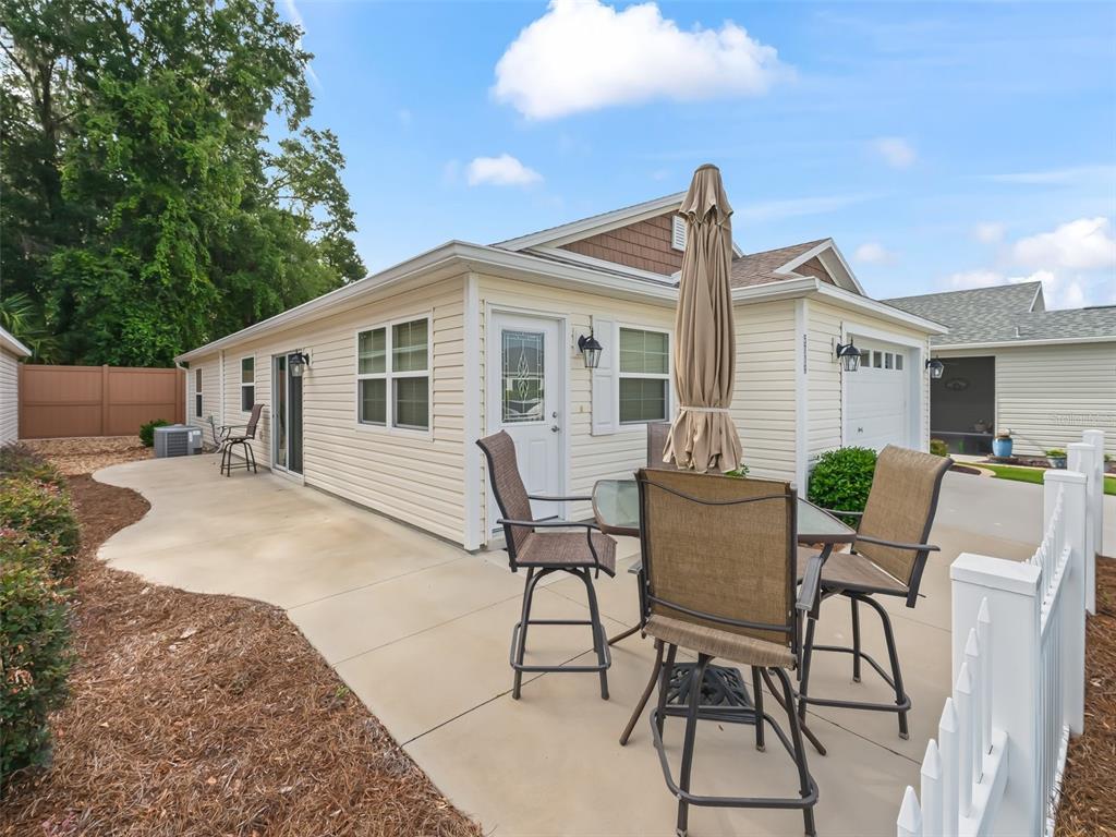 A patio with outdoor furniture sits beside a light-colored house with a garage — 5719 SPARTINA TERRACE, THE VILLAGES, FL