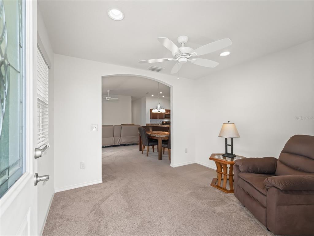 A carpeted living room features a brown recliner, a side table, and an arched entryway — 5719 SPARTINA TERRACE, THE VILLAGES, FL