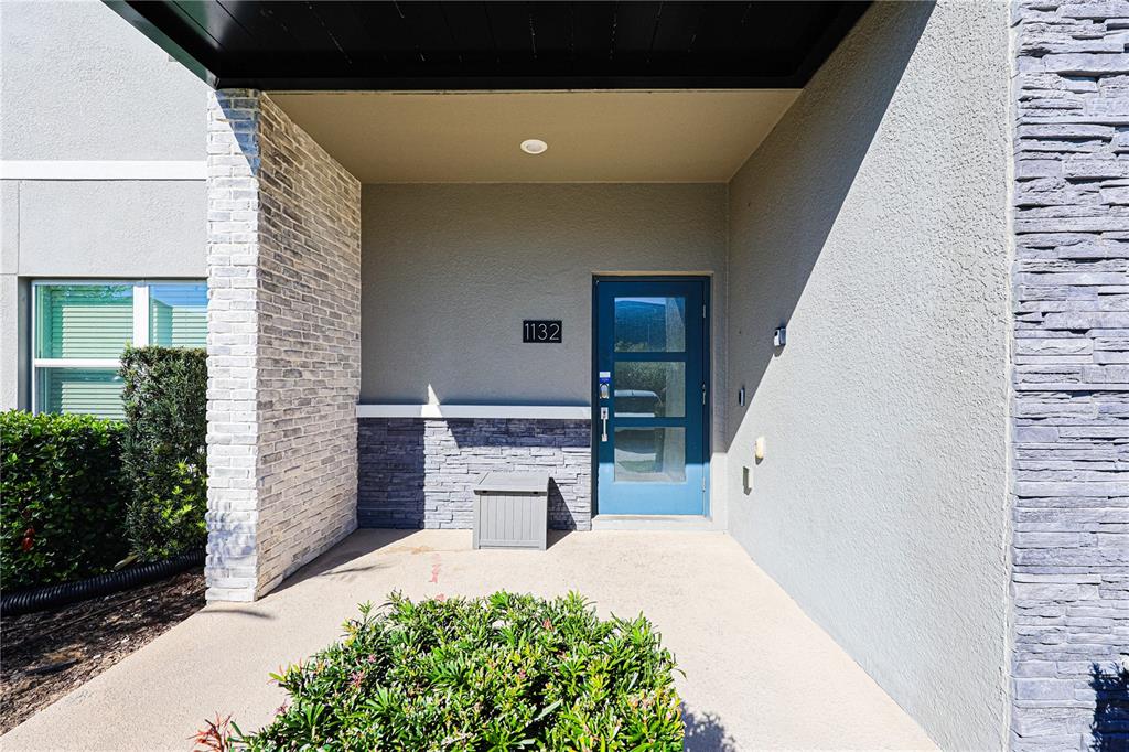 A blue front door with glass panels sits under a covered porch with stone accents — 1132 CHALLENGE DRIVE, DAVENPORT, FL