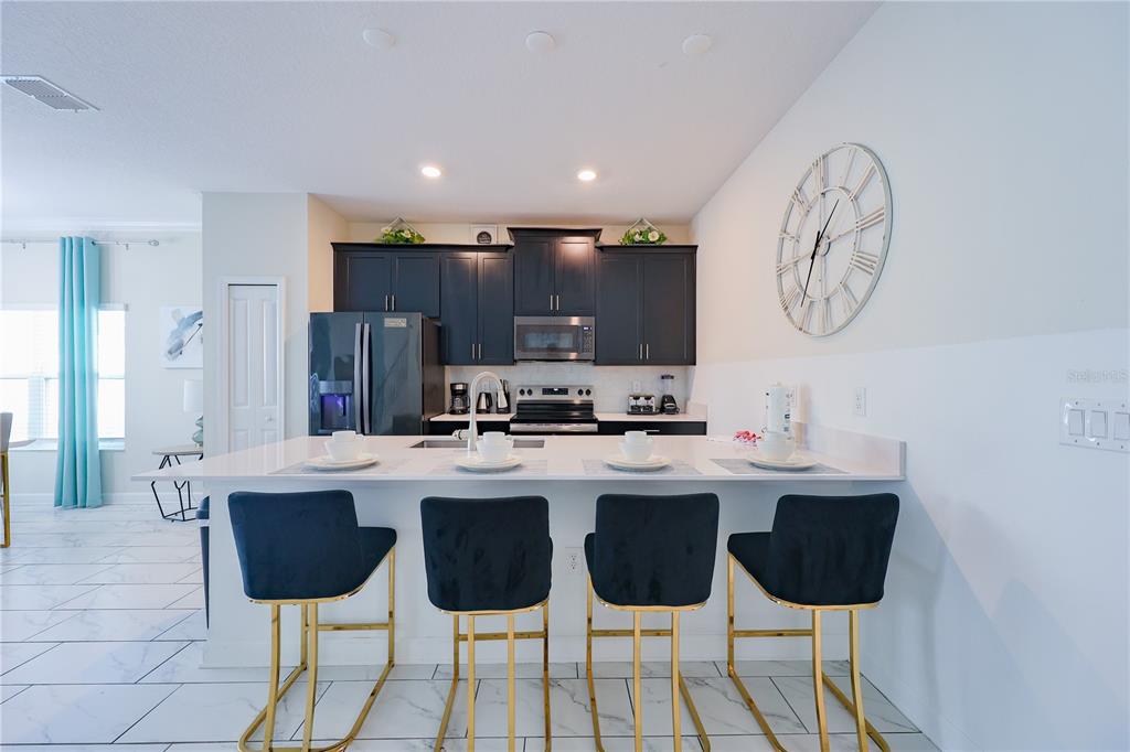 A kitchen features dark cabinets, a white island with four bar stools, and marble-look flooring — 1132 CHALLENGE DRIVE, DAVENPORT, FL