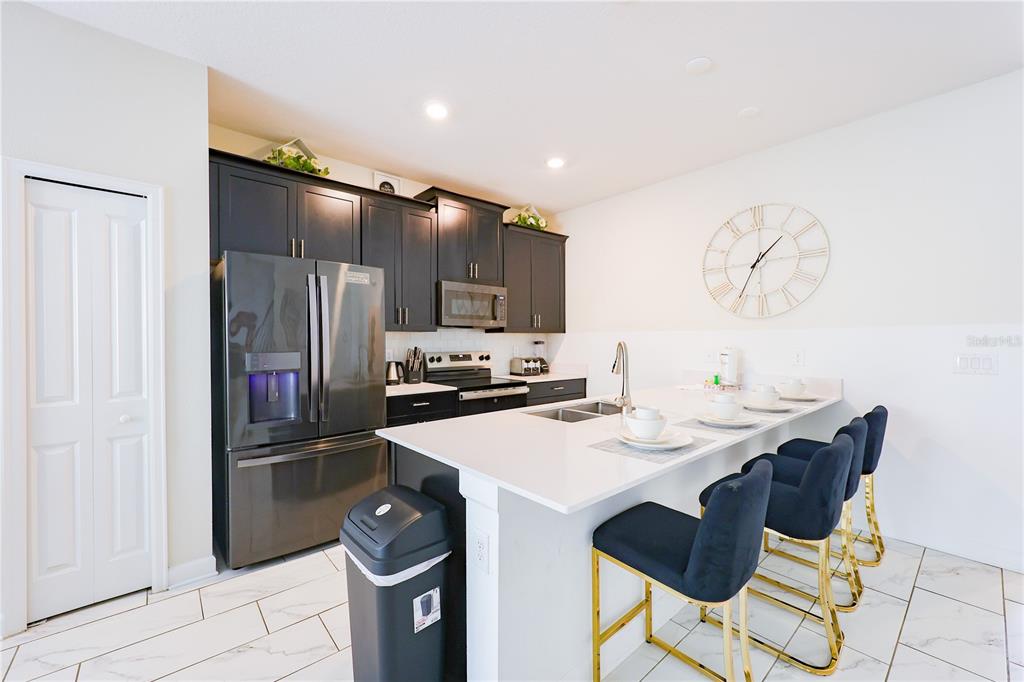 A modern kitchen features dark cabinets, stainless steel appliances, a white island, and bar stools — 1132 CHALLENGE DRIVE, DAVENPORT, FL