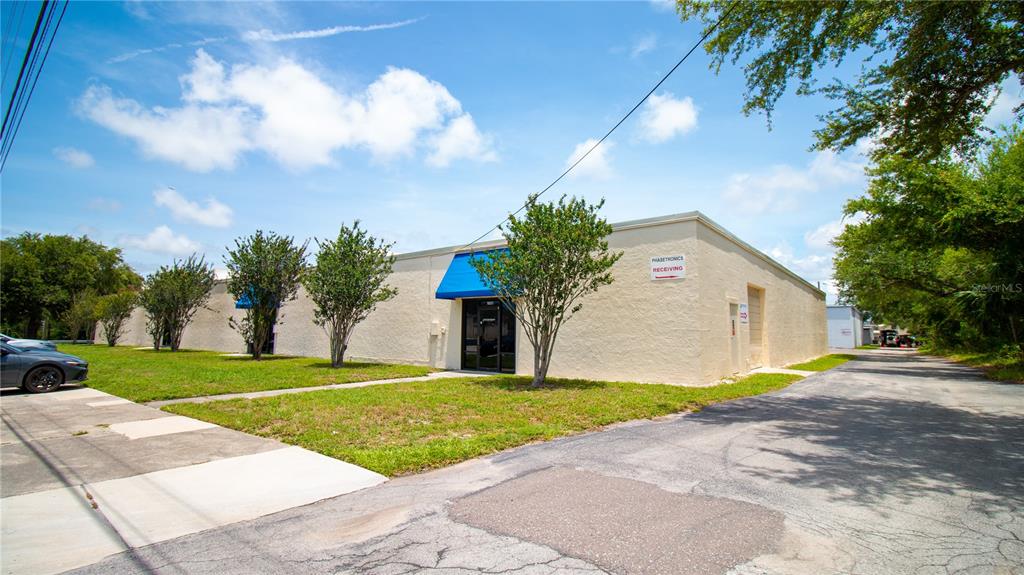 A low-rise commercial building with a tan stucco exterior and blue awnings sits on grass — 1603 SUNSHINE DRIVE, CLEARWATER, FL