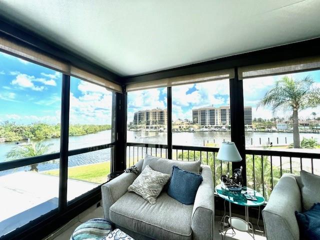 A sunroom features comfortable seating and large windows overlooking a waterfront view with distant buildings — 3270 SOUTHSHORE DRIVE UNIT 72B, PUNTA GORDA, FL