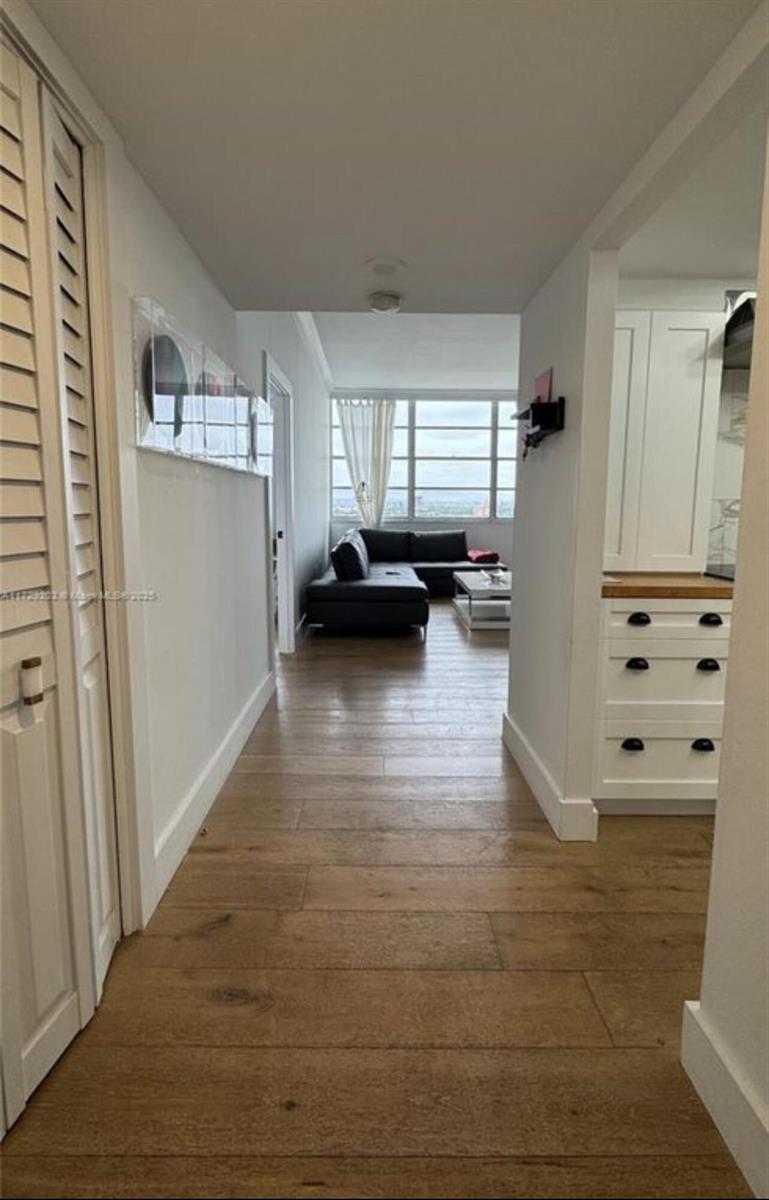 A hallway with light wood flooring leads to a living room with a dark sectional sofa — 11930 N Bayshore Drive, North Miami FL 33181, NORTH MIAMI, FL