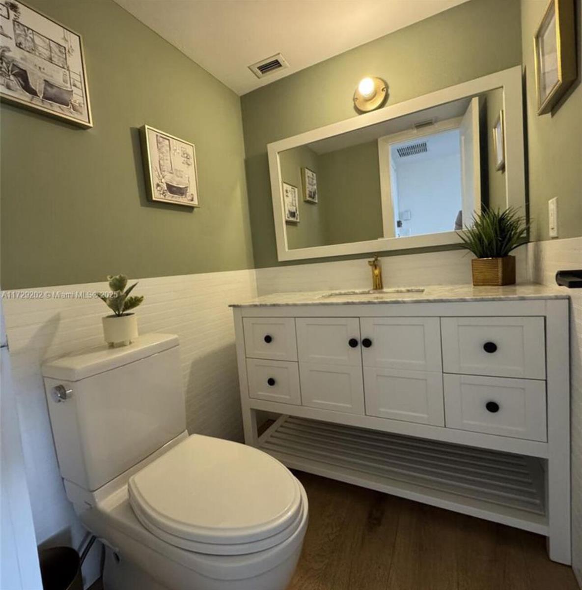 A bathroom features a white vanity, a toilet, and sage green walls with white wainscoting — 11930 N Bayshore Drive, North Miami FL 33181, NORTH MIAMI, FL