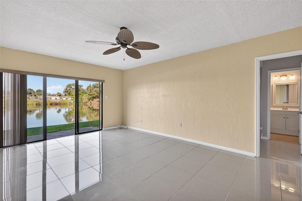 A living room with light-colored tile floors, a ceiling fan, and sliding doors overlooking water — 1749 S HIGHLAND AVENUE UNIT A5, CLEARWATER, FL
