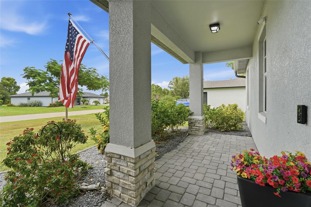 A paved front porch features stone-based columns, a hanging American flag, and potted flowers — 16146 GALIANO COURT, PUNTA GORDA, FL