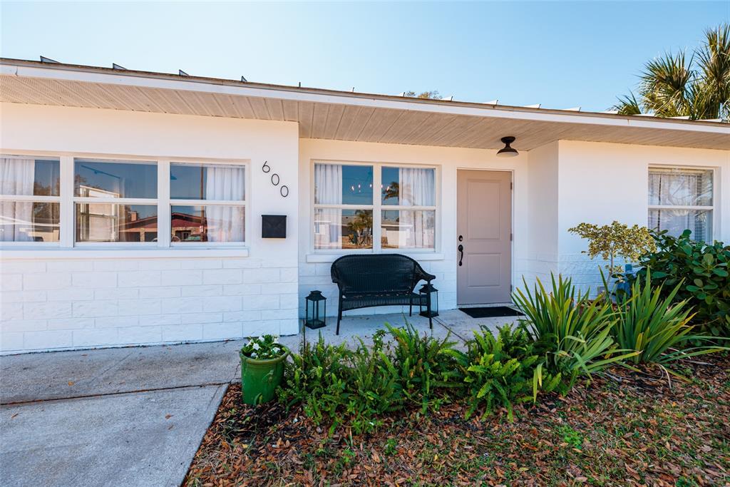 The exterior of a white, single-story house features a front porch with a black bench — 600 74TH AVENUE N, ST PETERSBURG, FL