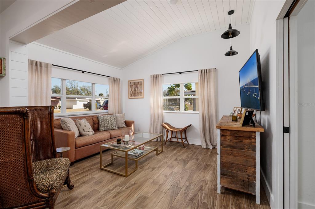 A living room features a vaulted ceiling, wood-look tile floors, and a brown sofa — 600 74TH AVENUE N, ST PETERSBURG, FL