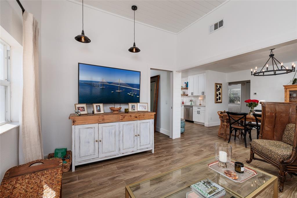 A living room with a television on a wooden cabinet, pendant lights, and wood-look flooring — 600 74TH AVENUE N, ST PETERSBURG, FL