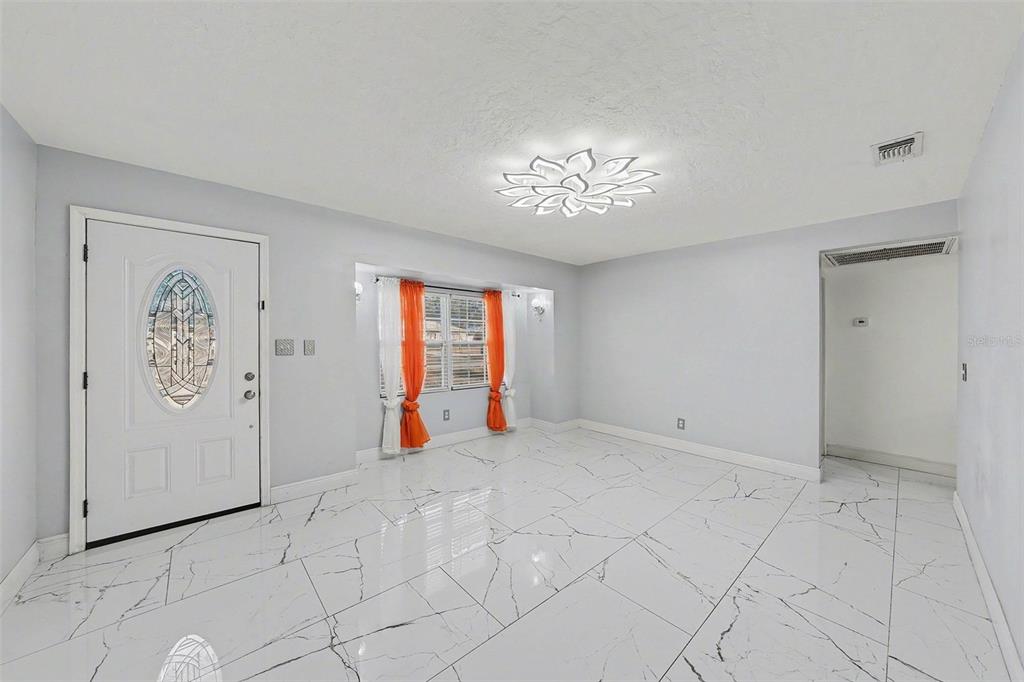 A bright room features white marble-look tile flooring, a floral ceiling light, and orange curtains — 2910 W BURKE STREET, TAMPA, FL