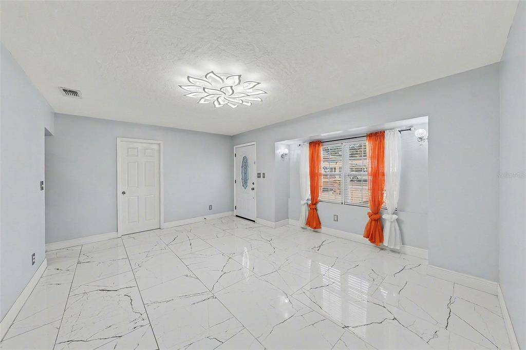 A bright room features white marble-look tile flooring, a floral ceiling light, and orange curtains — 2910 W BURKE STREET, TAMPA, FL