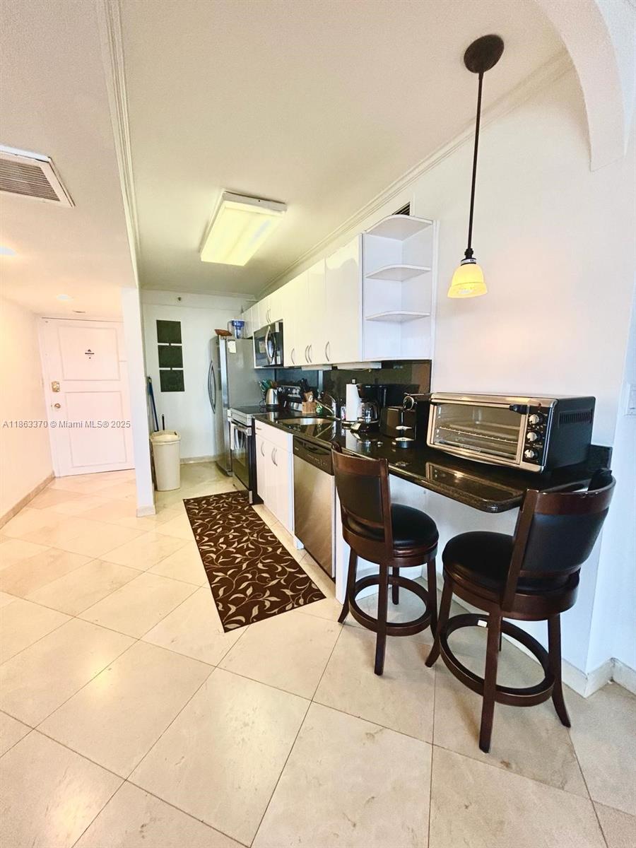 A galley kitchen features white cabinets, dark countertops, a breakfast bar, and tile flooring — 100 Lincoln Rd # 1034, Miami Beach FL 33139, MIAMI BEACH, FL