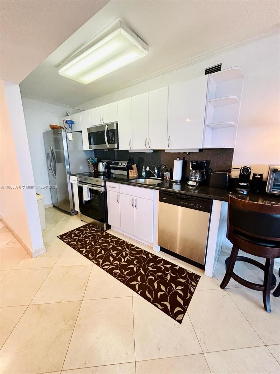 A kitchen features white cabinets, stainless steel appliances, dark countertops, and a patterned floor runner — 100 Lincoln Rd # 1034, Miami Beach FL 33139, MIAMI BEACH, FL