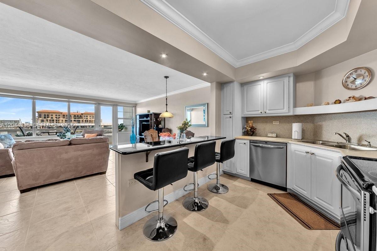 A kitchen with white cabinets and a breakfast bar overlooks a living area with balcony views — 3111 N Ocean Dr # 904, Hollywood FL 33019, HOLLYWOOD, FL