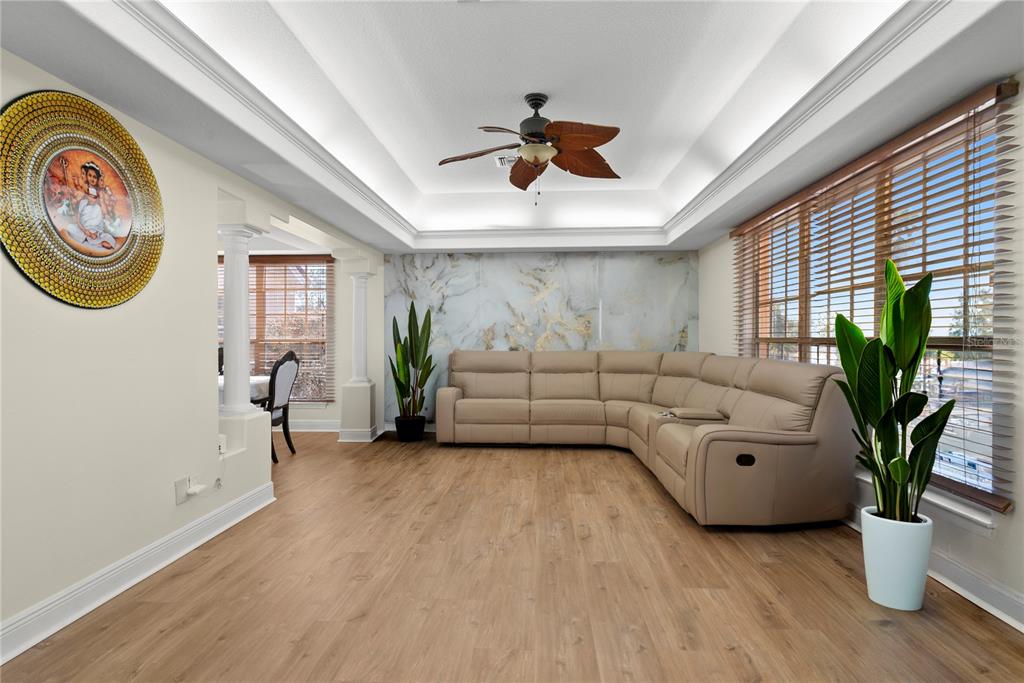A living room with wood-look flooring, a beige sectional sofa, and a marble-patterned accent wall — 16727 ROYAL PALM DRIVE, GROVELAND, FL