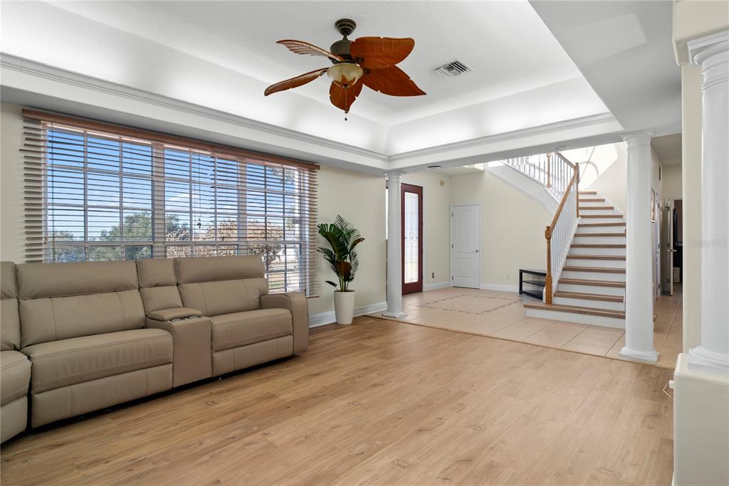 A living room with light wood flooring, a beige sofa, and a staircase in the background — 16727 ROYAL PALM DRIVE, GROVELAND, FL