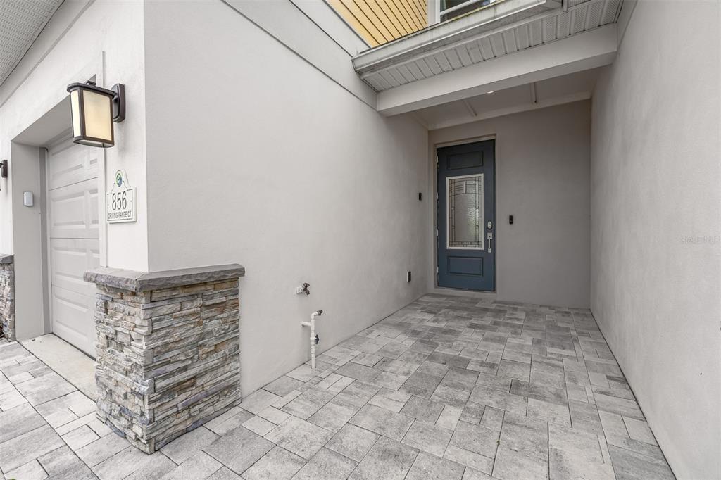 A paved entryway leads to a blue front door beside a garage with stone accents — 856 DRIVING RANGE COURT, REUNION, FL